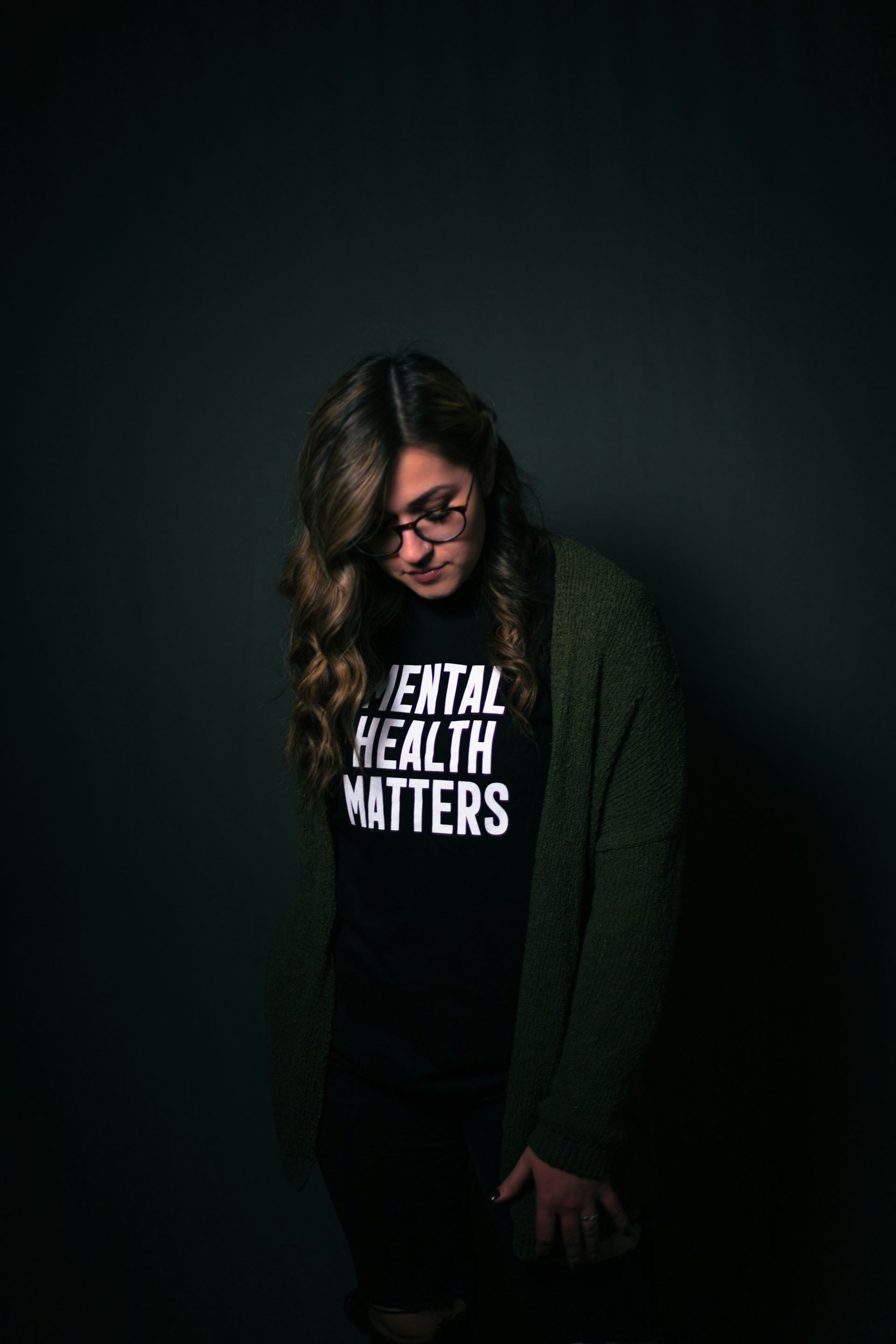 woman with long hair and glasses looking down wearing a black t shirt with white lettering 'mental health matters'